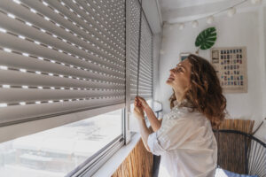 Young woman opening roller window on the balcony